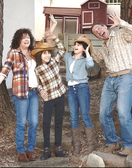 a family of four with mom, dad and two kids dressed in flannel shirts with their hands in the air
